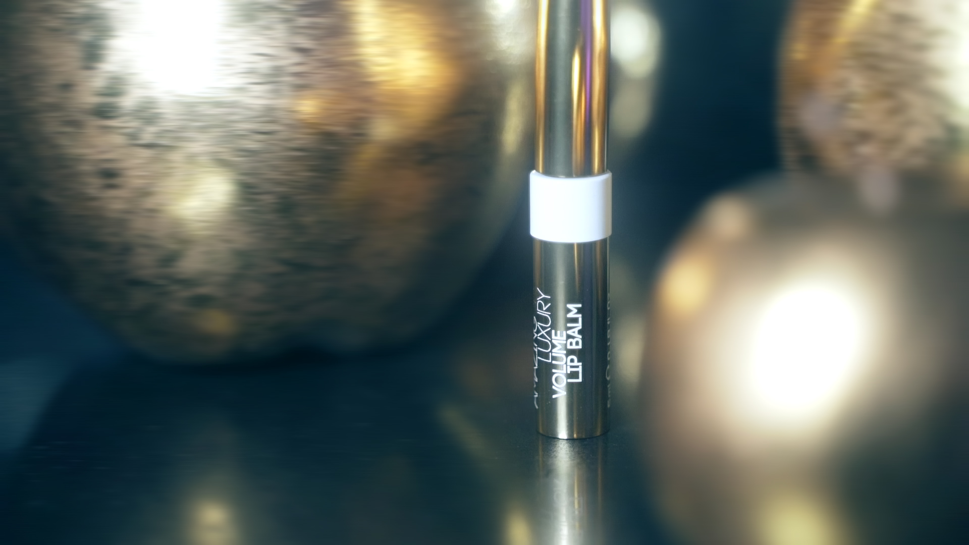 Close-up of a lip balm tube standing upright with a white band, set against a blurred metallic background.