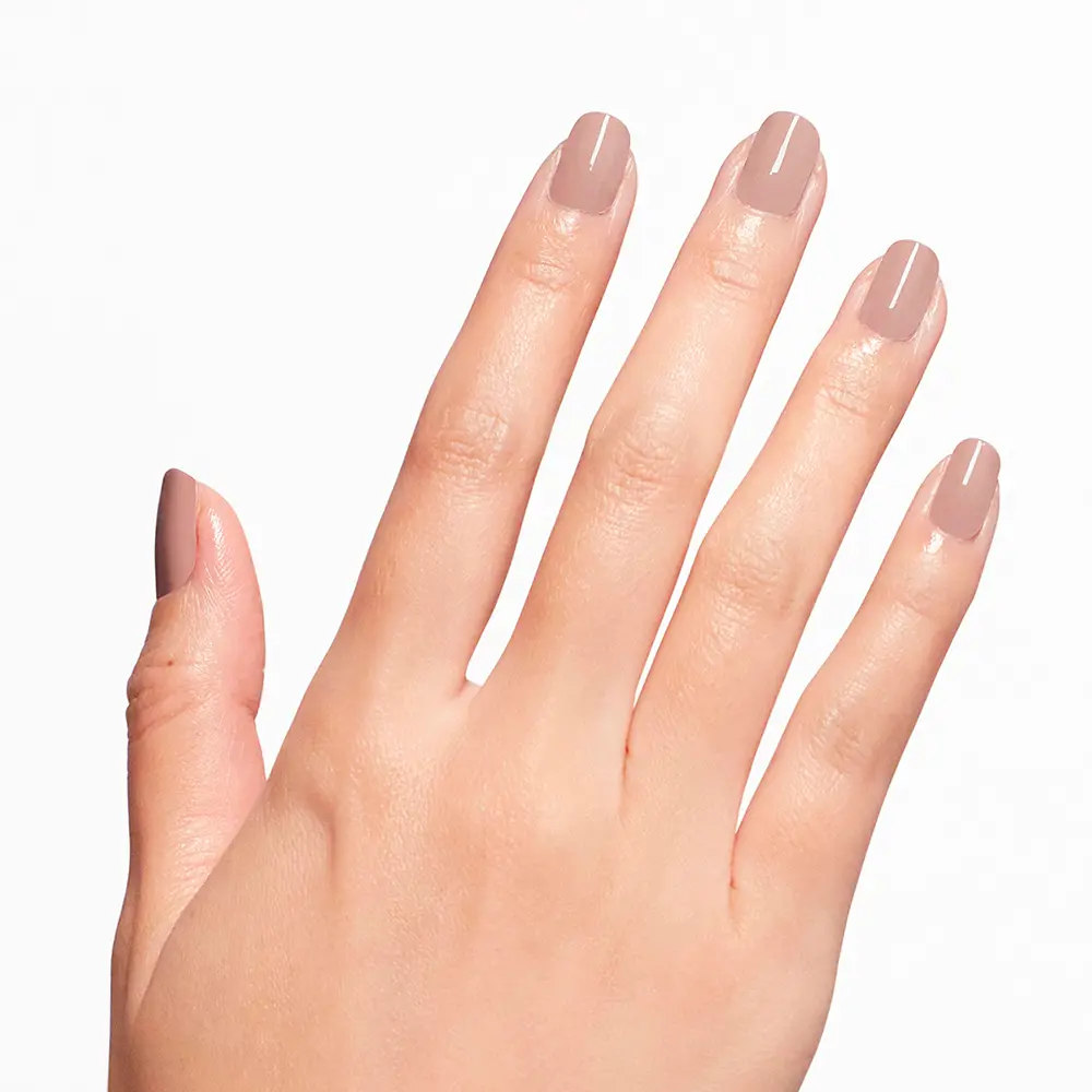 Close-up of a hand with nude pink manicure on short rounded nails, against a white background.