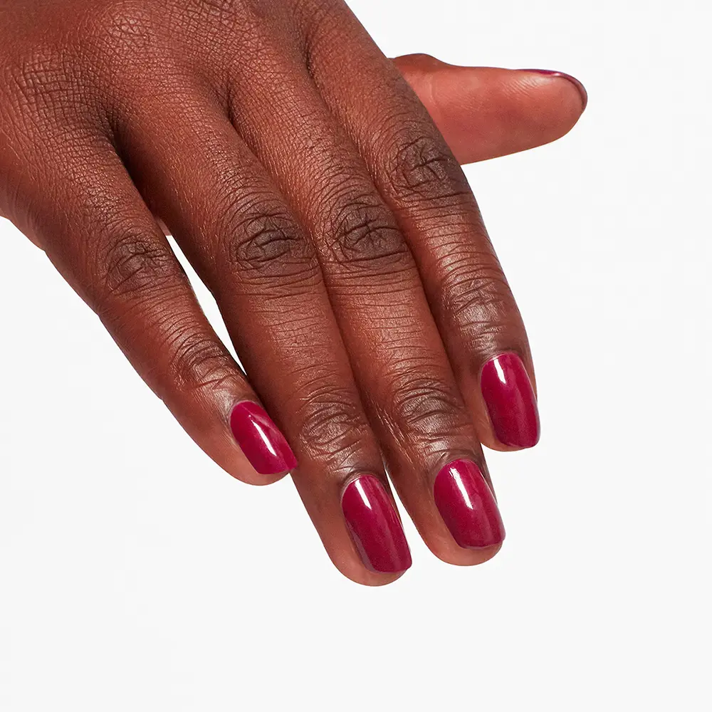 Close-up of a dark-skinned hand with magenta nail polish on all nails against a white background.