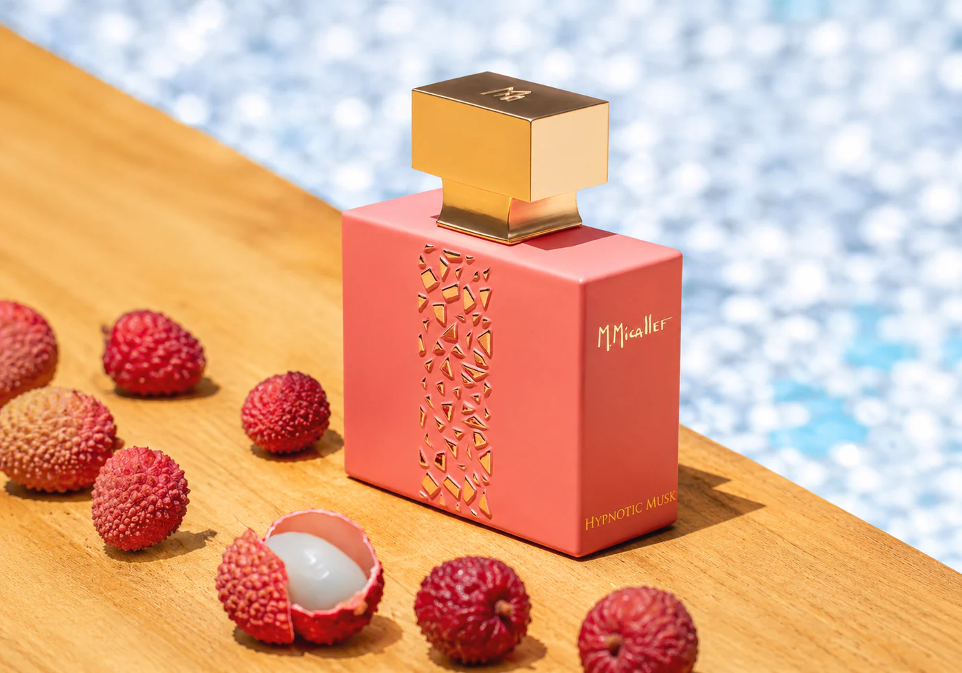 Pink rectangular perfume bottle with a gold square cap on a wooden surface, surrounded by raspberries. The bottle has a cutout pattern on the side and a mint label.
