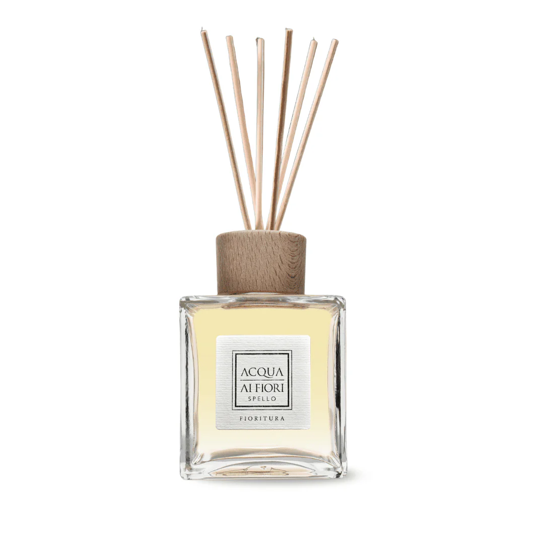 Glass square diffuser bottle with light yellow liquid, wooden cap, and several thin reed sticks fanning upward.