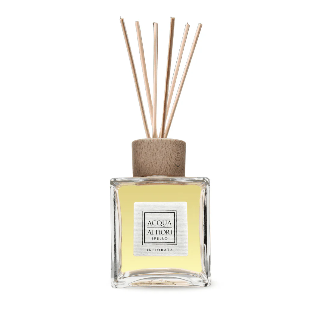 Square glass reed diffuser bottle with a wooden cap and light yellow fragrance liquid, beige reed sticks fanning upward.