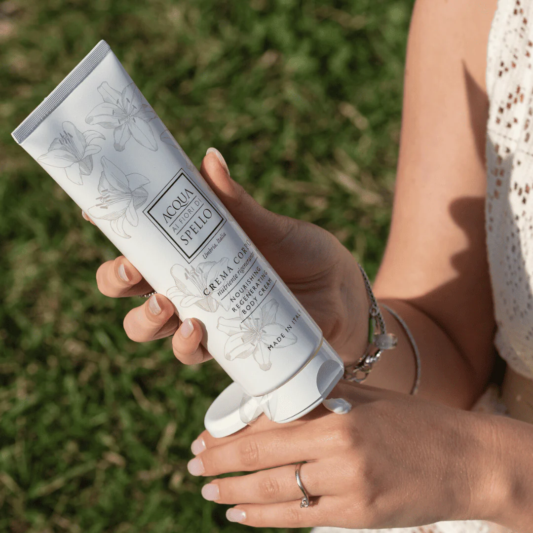 A person holding a white tube of lotion with floral designs outdoors, showing the brand label partially visible.