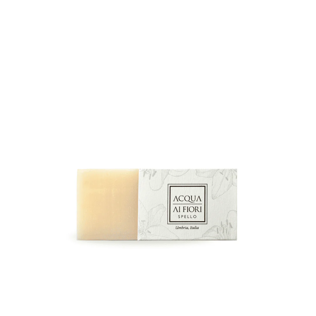 Soap bar with pale beige color beside a white decorative box featuring 'ACQUA AI FIORI' and 'Spello' text, Italy