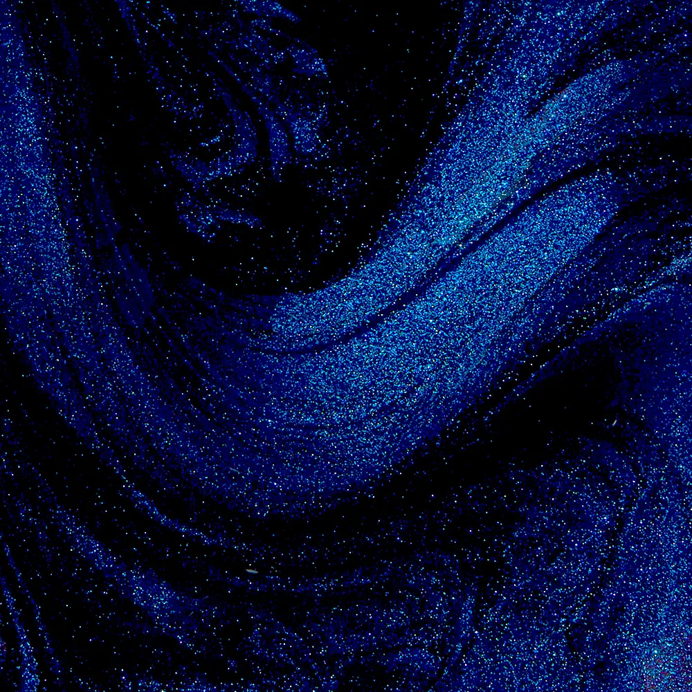Close-up of blue glitter swirling on a dark background to form flowing patterns gradually fading to black.