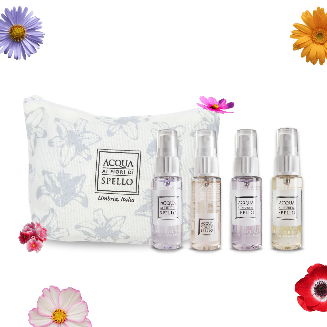Set of four Acqua ai Fiori di Spello perfume sprays beside a white floral pouch, with colorful flowers around.