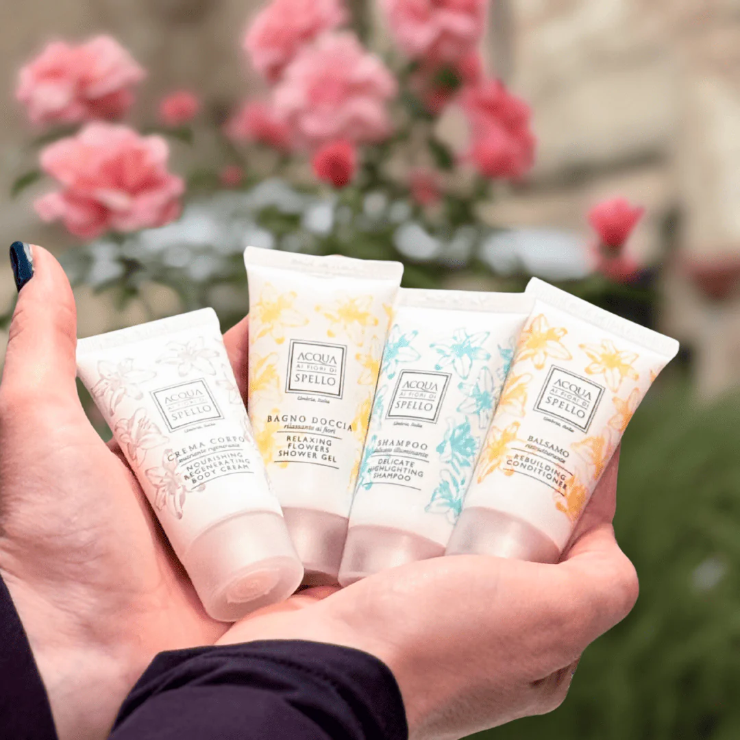 Hands holding four travel-size bath product tubes with floral pastel designs.