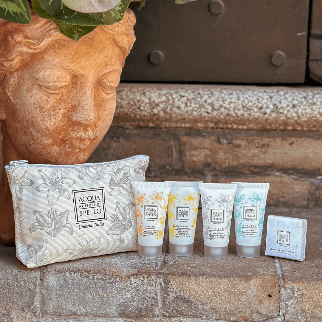 Travel-size skincare set with five tubes and a floral-patterned zip pouch resting on a stone step beside a clay bust planter.