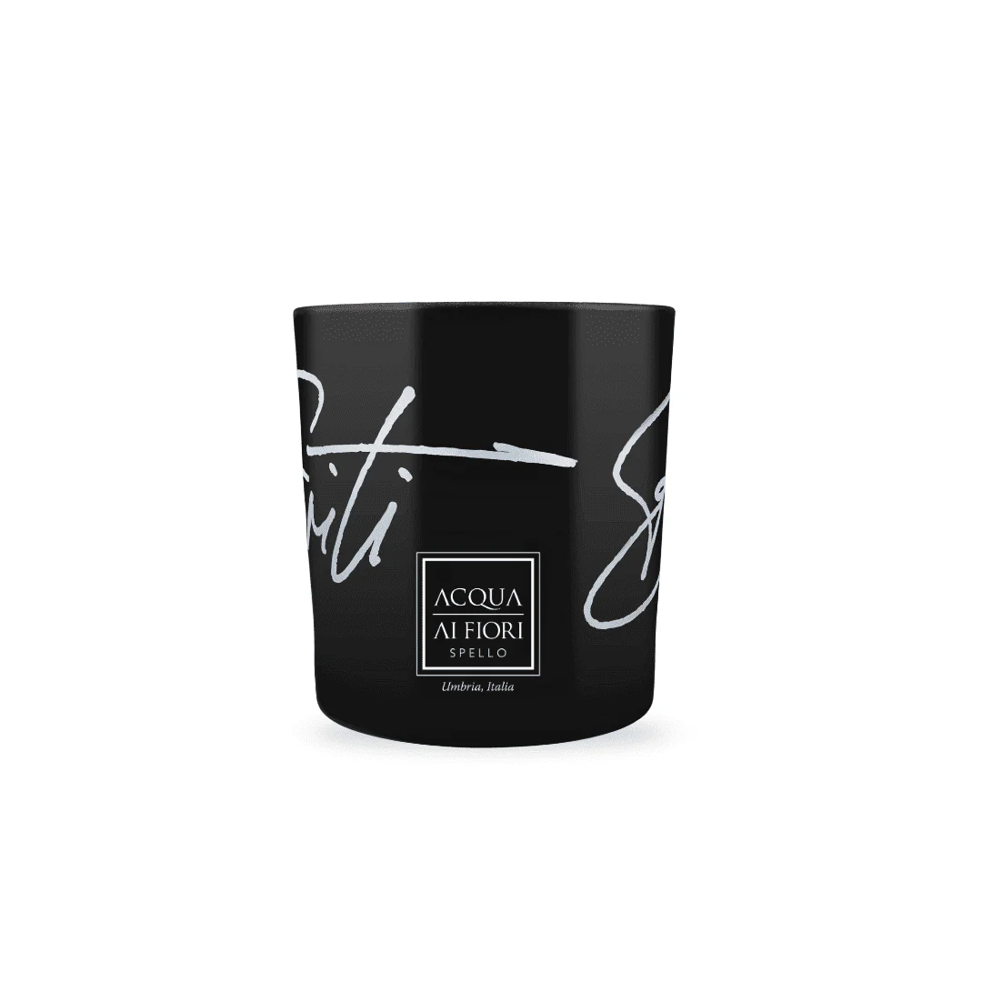 Black candle in a glossy black jar with white cursive text and a centered square label reading 'ACQUA AI FIORI SPELLO Umbria, Italia' on the front.