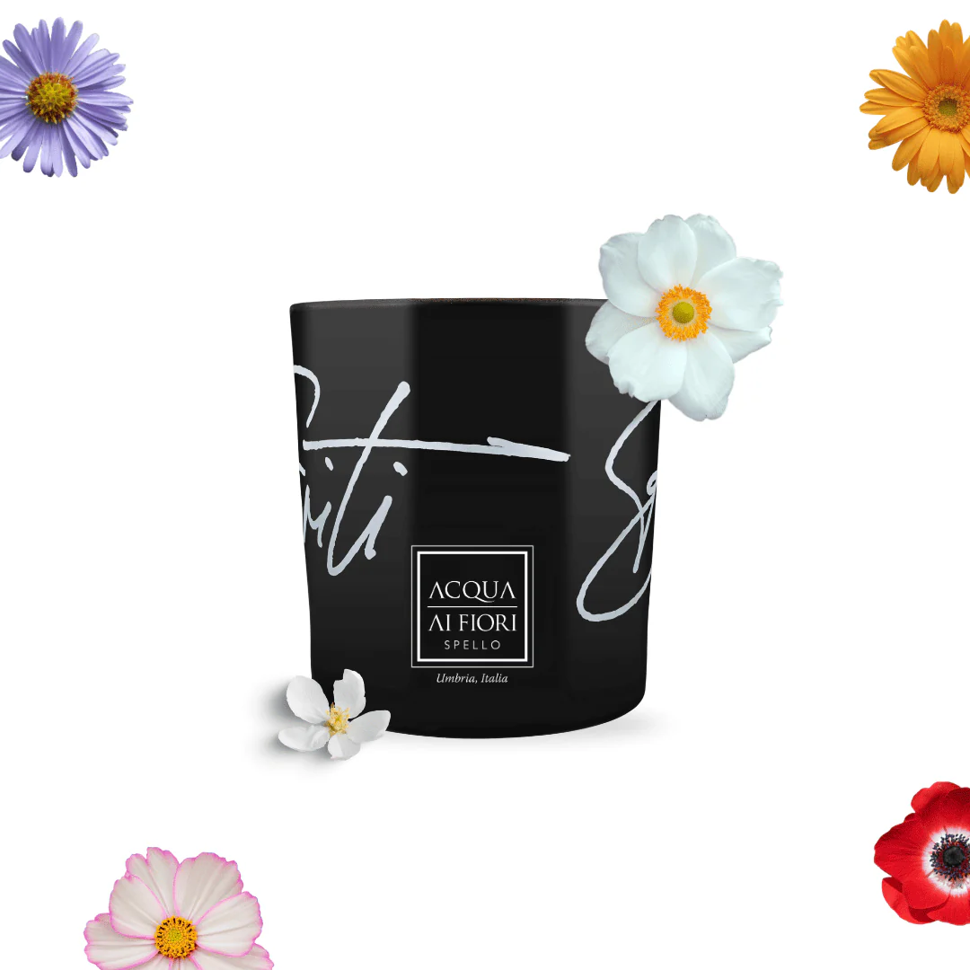 Black cylindrical container with white script and a square label, surrounded by colorful flowers on a white background.