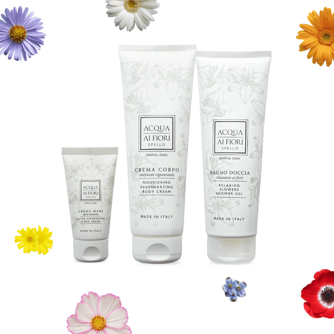Three Acqua Ai Fiori skincare tubes (hand cream, body cream, and shower gel) with botanical illustrations, displayed on a white background with colorful flowers around them.