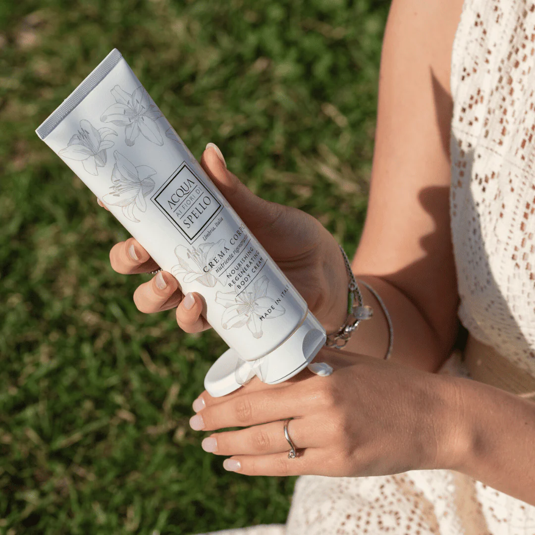 Woman holding a white floral-labeled lotion tube outdoors, about to dispense cream from the cap.