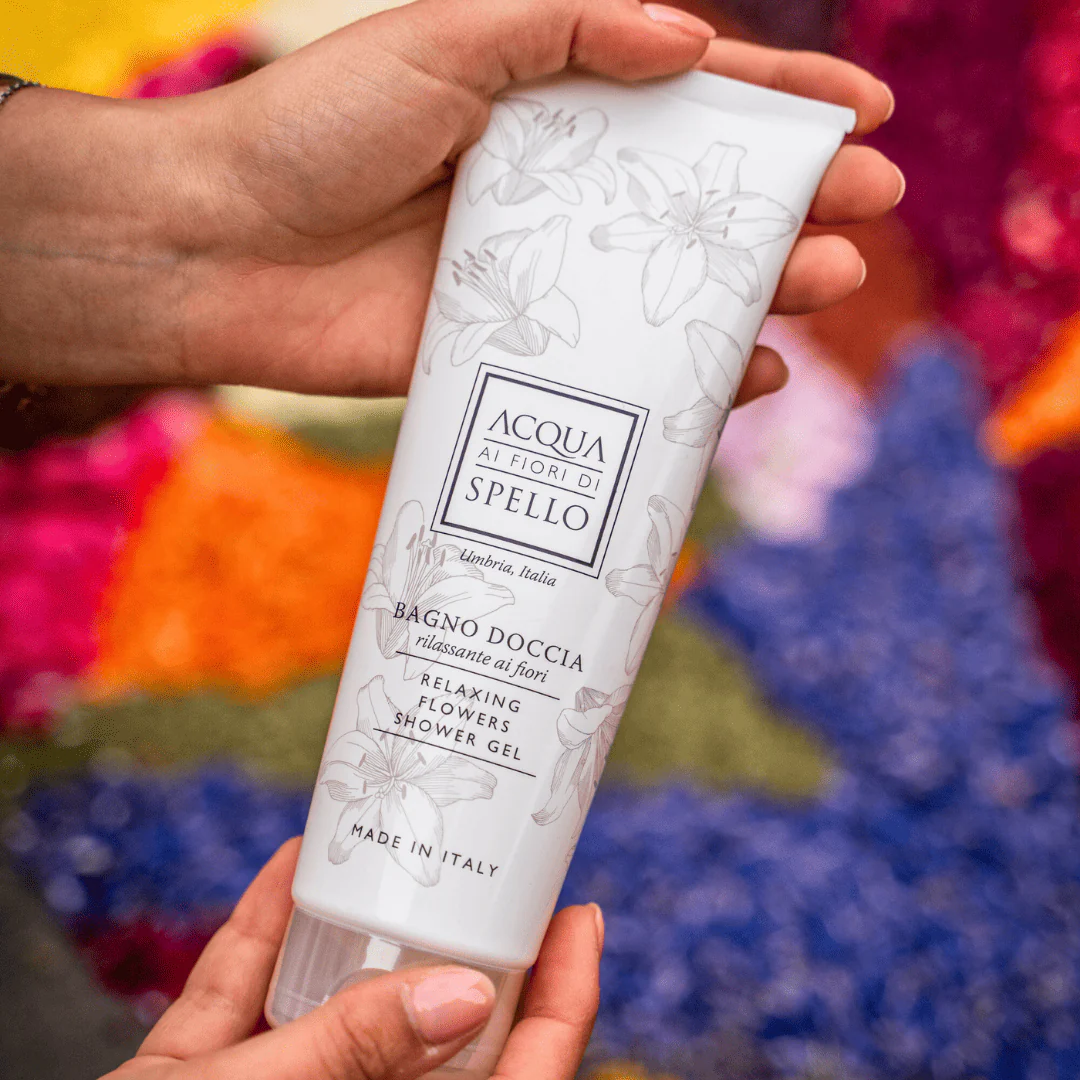 Hand holding a white bottle of Acqua ai Fiori di Spello Relaxing Flowers Shower Gel, with floral illustrations and 'Made in Italy' text on the label